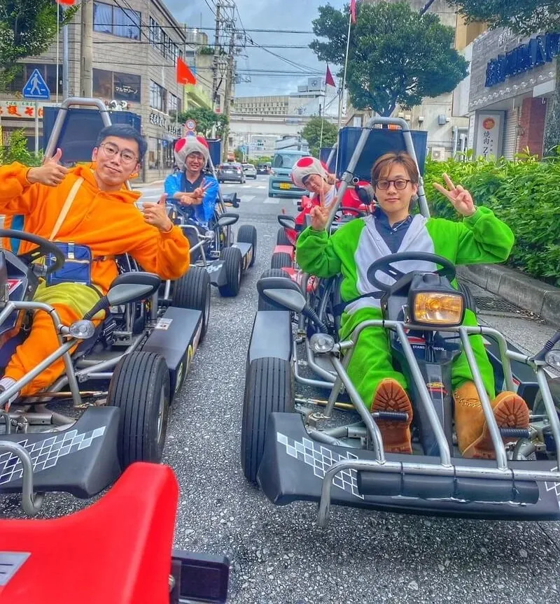 Two riders in orange and green cosplay at the wheel of Gorilla Karts on a Naha back street