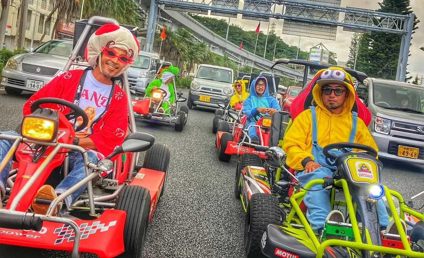 A red kart leading the convoy along a palm-lined road beneath the monorail