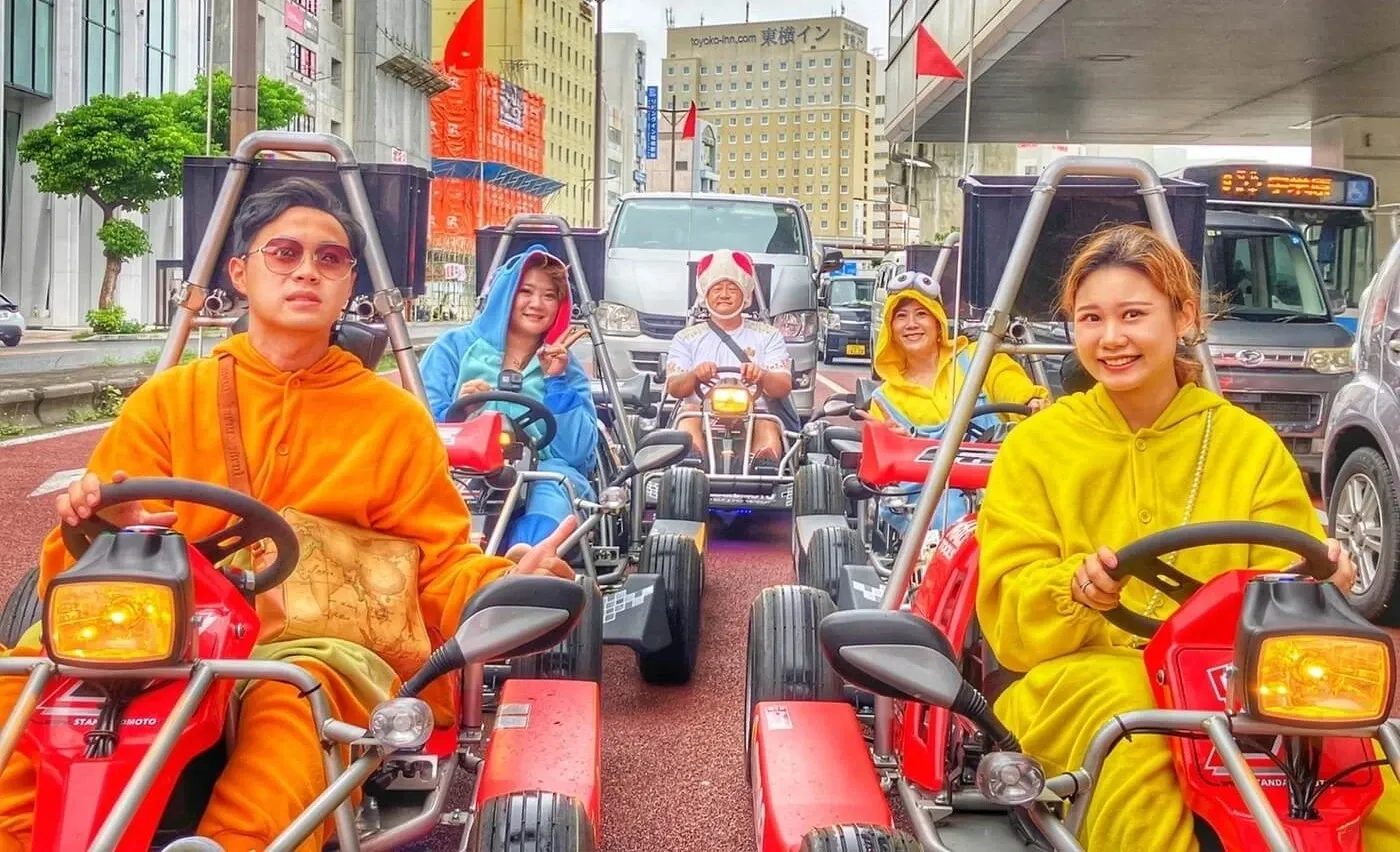 Three go karts in convoy on a wide Naha avenue beneath the monorail line