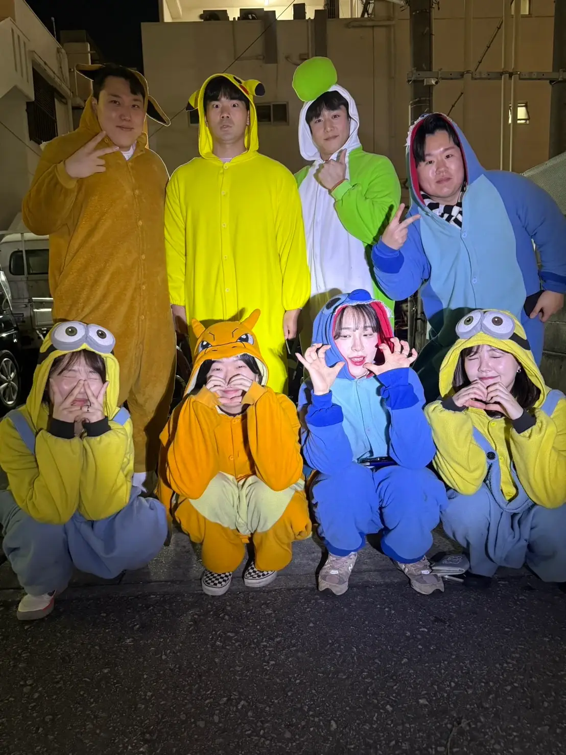 Eight riders in animal kigurumi posed in two rows on the forecourt after dark