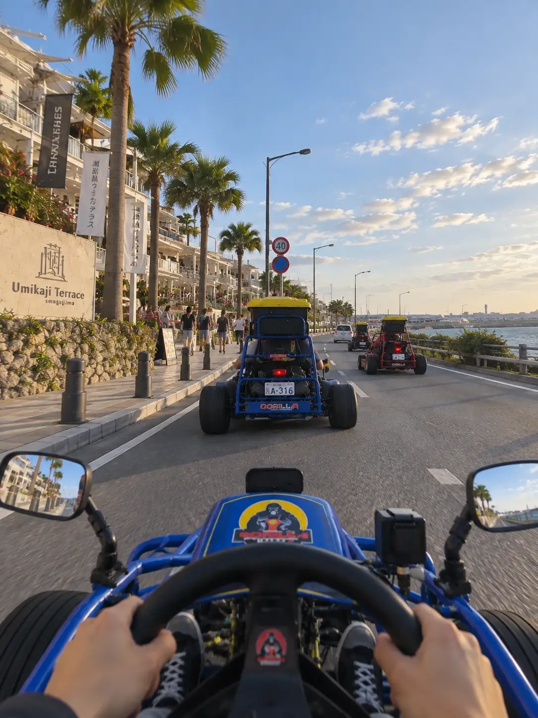 La vista desde detrás del volante de un kart de Gorilla Kart, recorriendo el paseo marítimo de Umikaji Terrace en la isla de Senaga al atardecer, con dos karts más delante