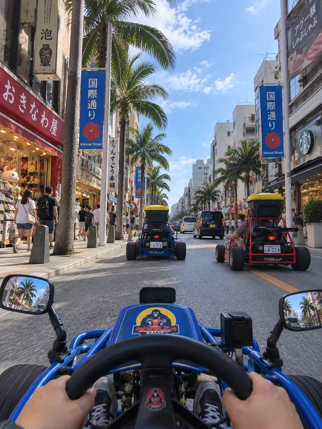 La vista desde detrás del volante de un kart de Gorilla Kart, bajando por Kokusai Dori en Naha, Okinawa, con dos karts más delante entre las tiendas y las palmeras