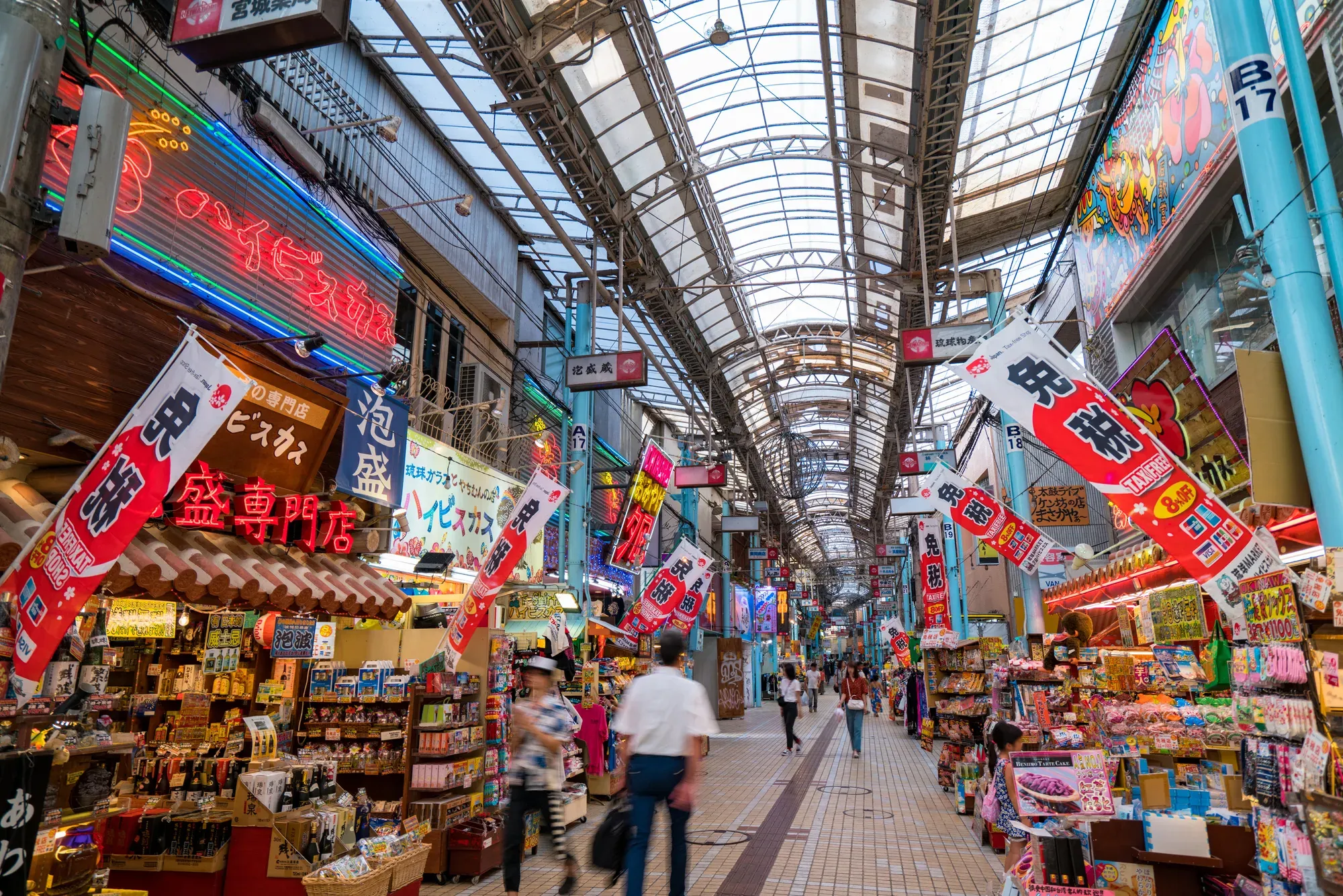 A covered shopping arcade in central Naha, souvenir shops on both sides under red and white banners
