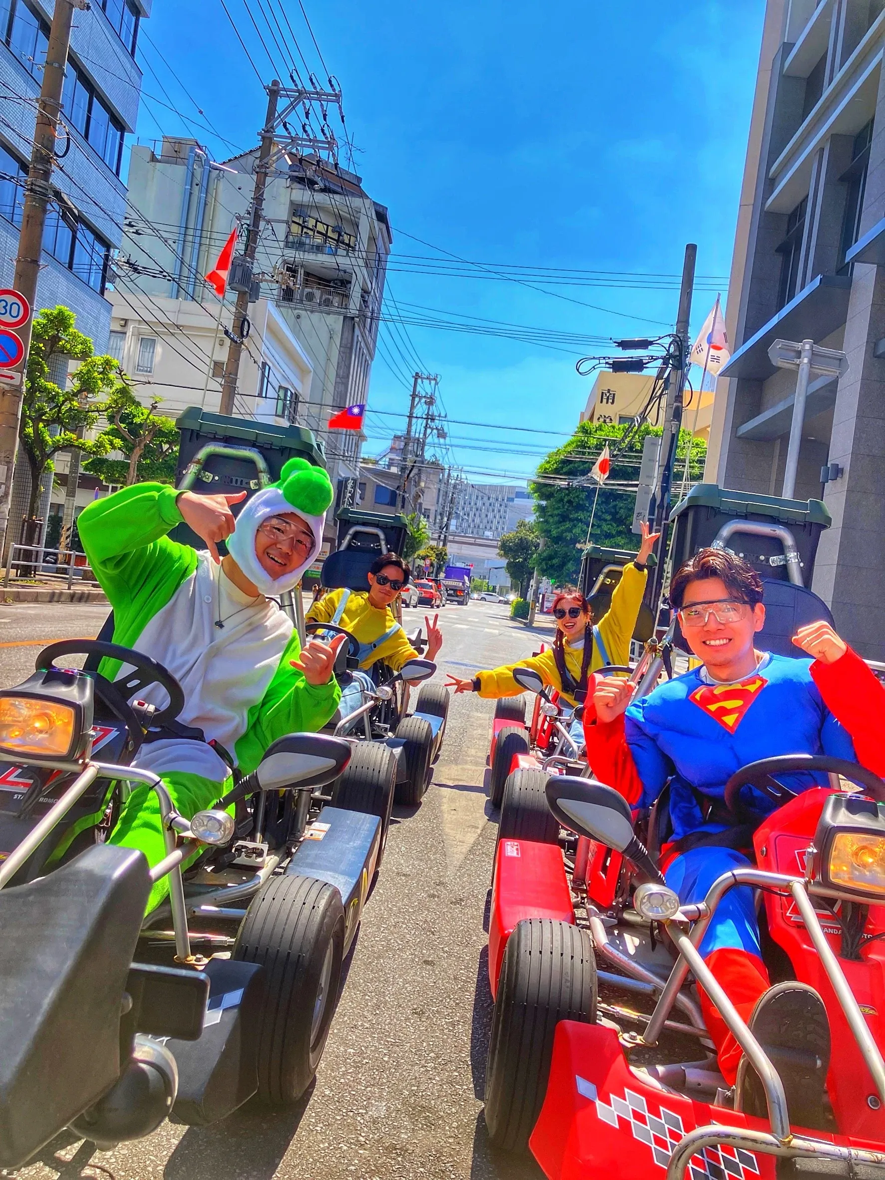 Riders in green kigurumi and a Superman costume at the wheel on a bright residential Naha street