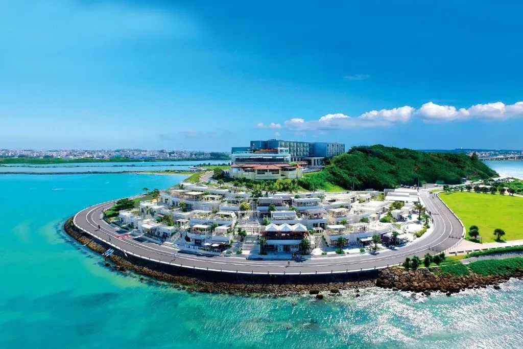 Senagajima from the air: Umikaji Terrace's white shops curving along the seawall, turquoise water around the island